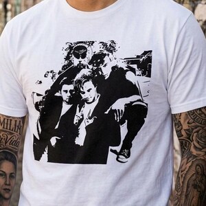 May include: A white ceramic mug with a black handle and the text "But First, Coffee" in a black, bold font. The mug is on a white surface.