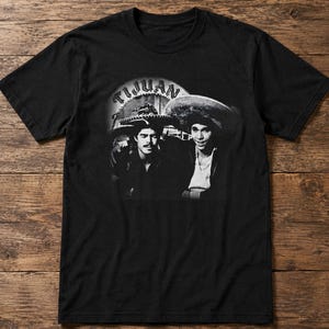May include: Black t-shirt featuring a black and white image of two men wearing hats, with the word "TIJUAN" in a circular design above them. The image is centered on the shirt.
