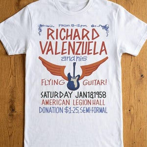 May include: A white short-sleeve t-shirt featuring a graphic print that reads: FROM 8-12pm. RICHARD VALENZUELA and his FLYING GUITAR! SATURDAY JAN 18 1958 AMERICAN LEGION HALL DONATION $1.25, SEMI-FORMAL. The design includes a blue guitar with orange wings.