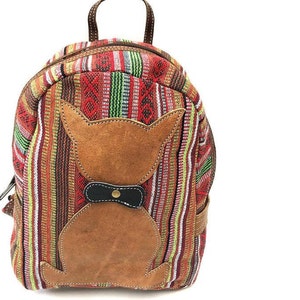 May include: A small, red, green, and yellow striped backpack with a brown leather cat appliqué. The cat has a black bow tie with a gold button.