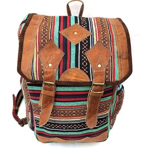 May include: A brown leather backpack with a colorful striped fabric front. The backpack has two large buckles and a diamond-shaped leather patch on the front.