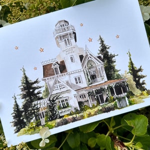 May include: Watercolour painting of a white house with a tower, surrounded by trees and stars. The text "There's a little witch in all of us" is written on the side of the house.