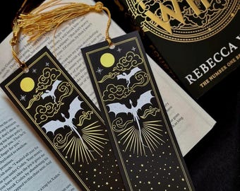 May include: Two black bookmarks with gold accents featuring a white dragon flying through clouds and stars. The text on the bookmarks reads "should I get the wingleader" and "should I wing".