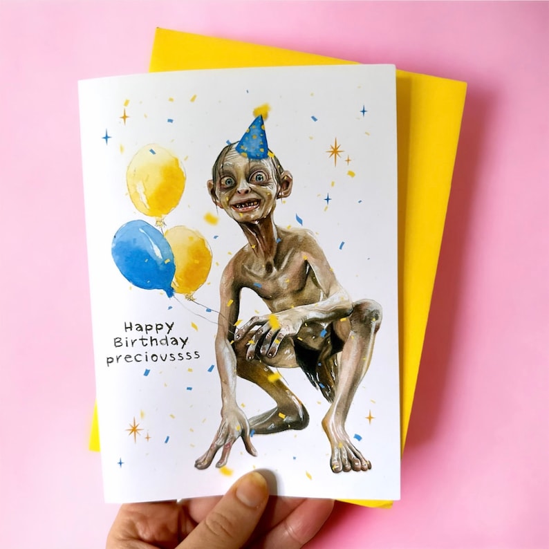 Puede incluir: Una tarjeta de cumplea&ntilde;os con una ilustraci&oacute;n de dibujos animados de Gollum de El Se&ntilde;or de los Anillos con un gorro de fiesta y sosteniendo globos. La tarjeta dice "Happy Birthday Precioussss".