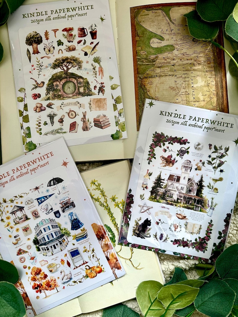 Peut inclure: Plusieurs inserts Kindle Paperwhite avec des illustrations. L'un d'eux pr&eacute;sente une carte, tandis que d'autres pr&eacute;sentent des autocollants th&eacute;matiques avec des images d'un trou de hobbit, d'une maison et d'autres &eacute;l&eacute;ments d&eacute;coratifs. Le texte "KINDLE PAPERWHITE" est visible.