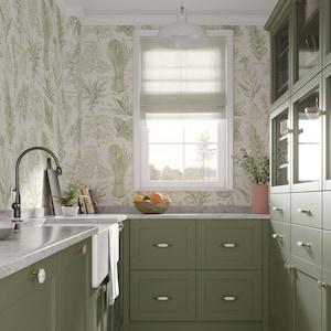 May include: A kitchen with green cabinets and a white farmhouse sink. The walls are covered in a botanical wallpaper with a light green and white pattern. The kitchen has a window with a white roman shade and a view of trees. There is a bowl of fruit on the counter.