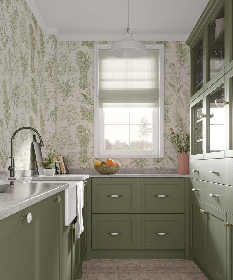 May include: A kitchen with green cabinets and a white farmhouse sink. The walls are covered in a botanical wallpaper with a light green and white pattern. The kitchen has a window with a white roman shade and a view of trees. There is a bowl of fruit on the counter.