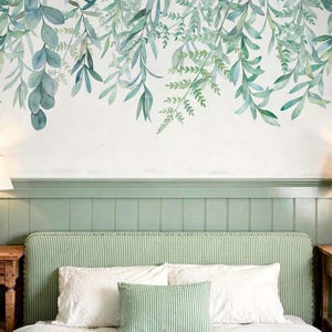 May include: A wall decal featuring a watercolor illustration of hanging eucalyptus and fern branches in various shades of green and teal. The botanical design is arranged to drape downward, creating a natural foliage pattern on a white wall.