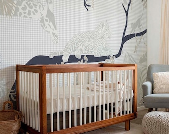 May include: A wooden crib with white vertical slats and a white mattress, positioned in front of a wall covered in wallpaper featuring a light gray gingham pattern and dark gray illustrations of a giraffe, a leopard, and monkeys on tree branches.