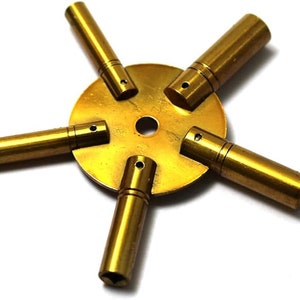 May include: A brass watch key winding tool with five different sized keys attached to a round base. The keys are used to wind different types of watches.