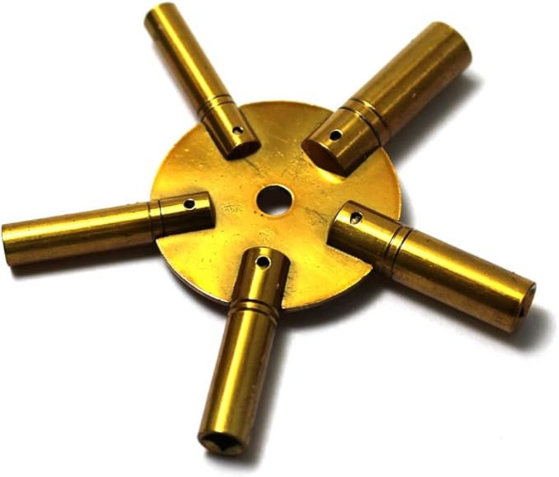 May include: A brass watch key winding tool with five different sized keys attached to a round base. The keys are used to wind different types of watches.