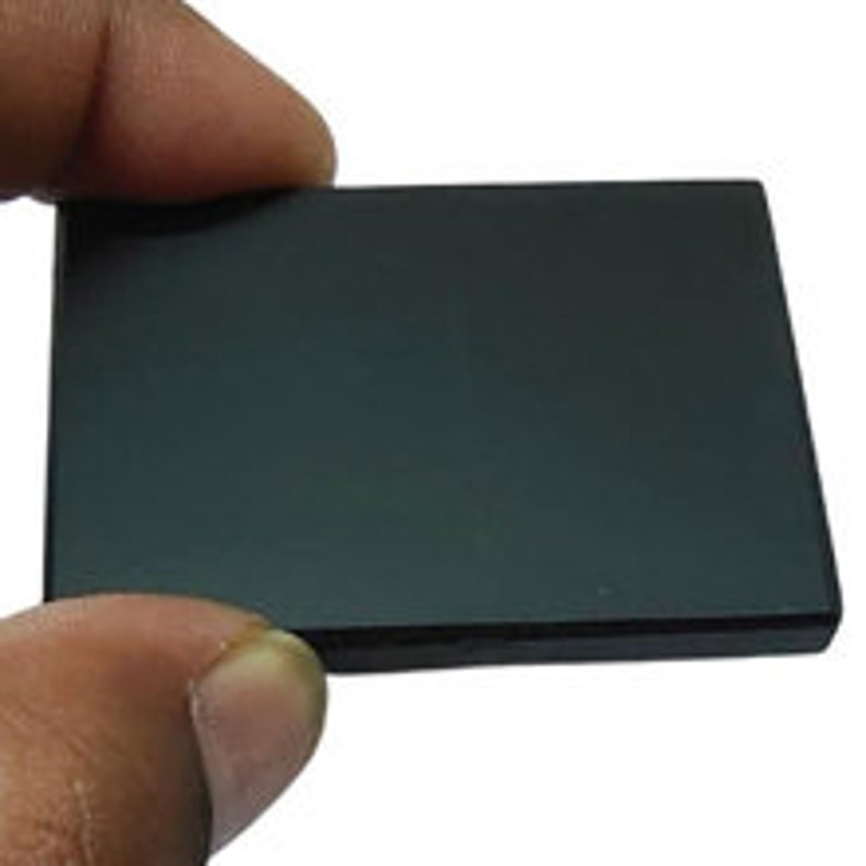 May include: A rectangular, black, polished stone held between fingers. The stone has a smooth, reflective surface. The edges of the stone are slightly beveled. The stone is approximately 3 inches long and 2 inches wide.