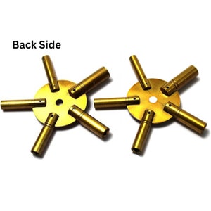May include: A set of two gold-colored watch key winders with six different sized prongs. The prongs are arranged in a star shape around a central disc. The text "Back Side" is visible in the image.
