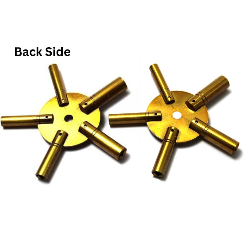 May include: A set of two gold-colored watch key winders with six different sized prongs. The prongs are arranged in a star shape around a central disc. The text "Back Side" is visible in the image.