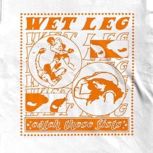 Pode incluir: Camiseta branca com um design gráfico laranja. O design inclui o texto "WET LEG" acima de três ilustrações circulares e a frase "catch these fists" abaixo. As ilustrações retratam figuras em ação.