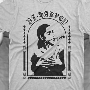 Könnte beinhalten: Hellgraues T-Shirt mit einem schwarzen Grafikdesign. Das Design zeigt eine Person mit einem Musikinstrument und den Text "DJ-HARVED" in einem bogenförmigen Rahmen. Das T-Shirt hat kurze Ärmel und einen Rundhalsausschnitt.