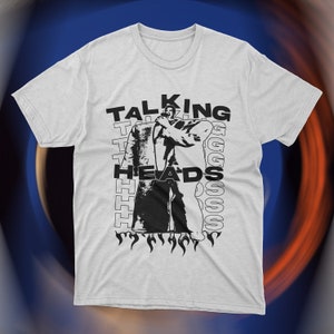Vintage-inspired white Talking Heads t-shirt featuring bold red graphic print of David Byrne in oversized suit with flames and repeating text design. Retro new wave band tee, unisex fit