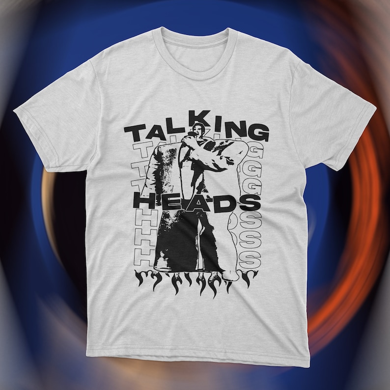Vintage-inspired white Talking Heads t-shirt featuring bold red graphic print of David Byrne in oversized suit with flames and repeating text design. Retro new wave band tee, unisex fit
