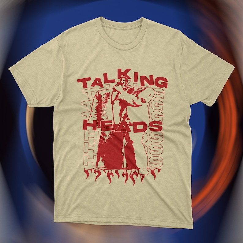 Vintage-inspired beige Talking Heads t-shirt featuring bold red graphic print of David Byrne in oversized suit with flames and repeating text design. Retro new wave band tee, unisex fit