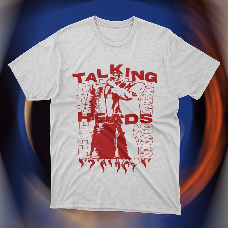 Vintage-inspired white Talking Heads t-shirt featuring bold red graphic print of David Byrne in oversized suit with flames and repeating text design. Retro new wave band tee, unisex fit