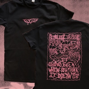 May include: Black t-shirts with pink graphic designs. One shirt has a small mouth-like design on the front. The other shirt has the text "INLIGENCE IS LIKE FOOD BETWEEN YOUR TEETH IT SHOWS EVEN WHEN YOU THINK IT DOESN'T" in a pink, chain-like design.