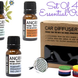 May include: Set of four 10 ml amber glass bottles of essential oils for car diffusers, labelled with different scents: Travel Ease, Focus & Drive, Traffic Jam, and Long Drive. The bottles are arranged in a row on a white background. A brown cardboard box with a clear window shows a silver car diffuser with a geometric design and ten colourful felt pads.