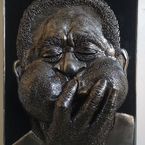 Puede incluir: Una escultura de metal en blanco y negro de un rostro humano con la mano cubriendo la boca. La escultura es texturizada y tiene un aspecto realista.