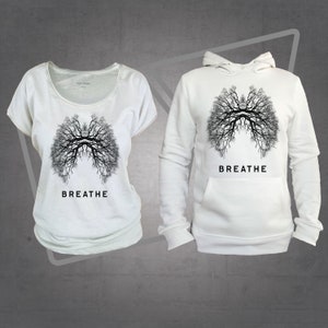 Może przedstawiać: Dwie białe koszulki z czarnym wzorem drzewa przypominającym płuca. Koszulki mają napis "BREATHE" wydrukowany pod wzorem.
