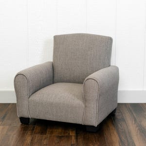 May include: A small, upholstered armchair featuring a textured, light gray fabric finish. The chair has a high, straight backrest, rounded armrests, and a low-profile seat cushion, supported by four short, dark-colored feet at the base.