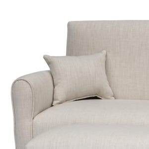 May include: A beige sofa with a textured fabric finish and a matching square throw pillow resting against the armrest. The sofa features a rounded arm design and a clean, neutral appearance with a consistent woven pattern across all surfaces.