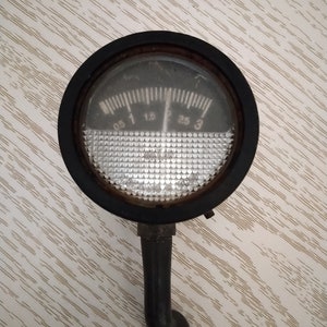 Può includere: Un manometro nero con un quadrante bianco e un ago nero. Il manometro è graduato da 0,5 a 3. Il manometro è fissato a un tubo di metallo nero.