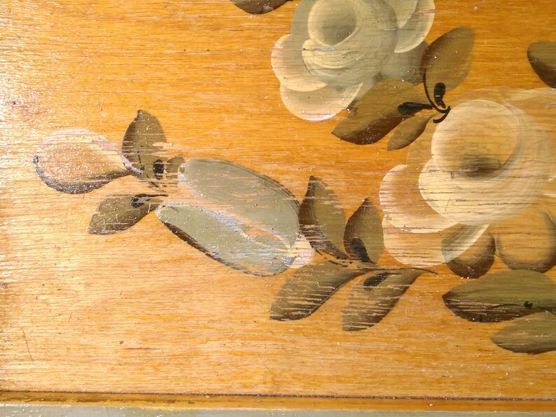 May include: A wooden surface with a painted floral design. The flowers are white with green leaves and are painted in a rustic style.