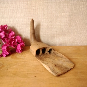 May include: A wooden carving shaped like a bird's head with a long beak and three holes in the top. The carving is brown and has a rough texture.