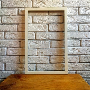 Può includere: Una cornice bianca su un muro di mattoni bianchi con un tavolo di legno in primo piano.