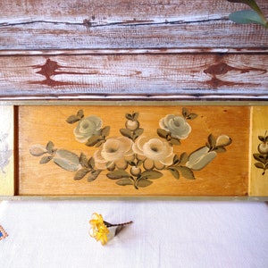 May include: A wooden tray with a painted design of white and green flowers. The tray is painted in shades of brown and yellow.