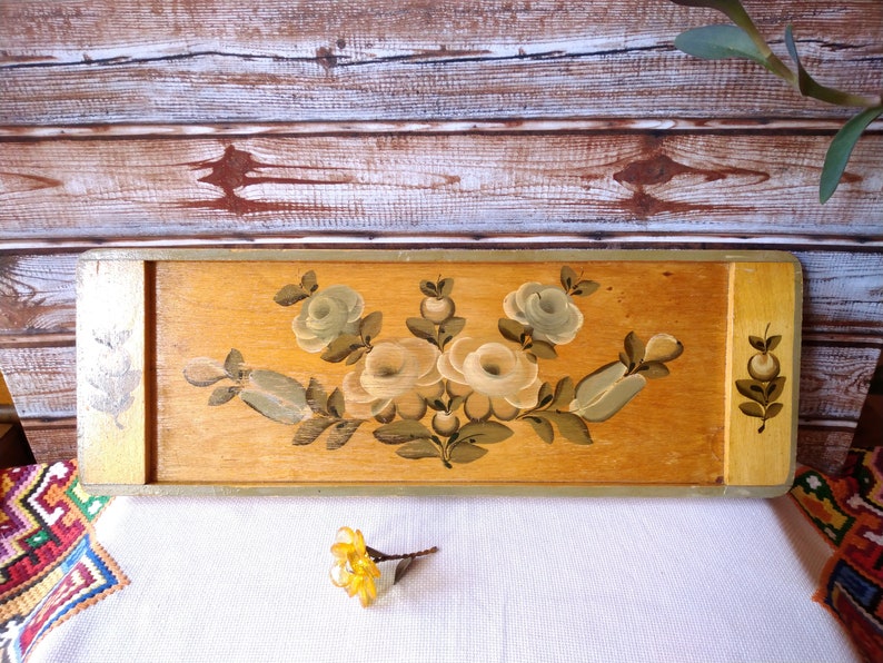 May include: A wooden tray with a painted design of white and green flowers. The tray is painted in shades of brown and yellow.