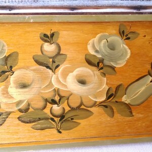 May include: A wooden panel with a hand-painted design of white roses and green leaves. The roses are painted in a realistic style with delicate details.