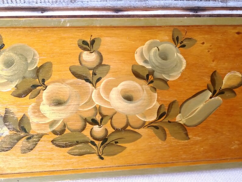 May include: A wooden panel with a hand-painted design of white roses and green leaves. The roses are painted in a realistic style with delicate details.