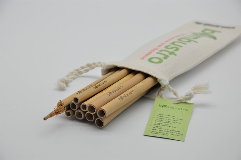 May include: A set of 12 natural bamboo straws in a white canvas bag with a drawstring closure. The bag has the text "bambustra" printed on it. The straws are bundled together and have the text "bambustra" printed on them.