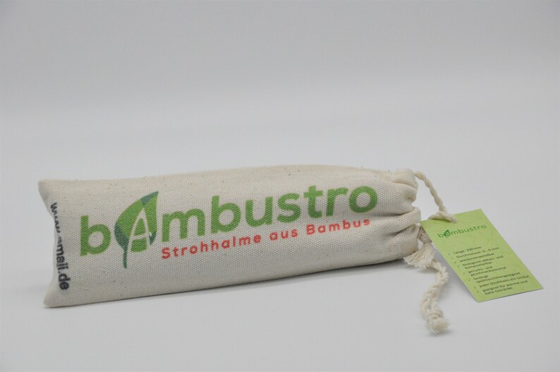 May include: A white canvas bag with a drawstring closure. The bag has a green logo that says "bambustro" and the text "Strohhalme aus Bambus". The bag is sitting on a white surface.
