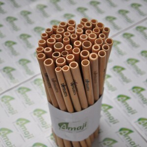 May include: A bundle of brown bamboo straws with the text "bambustro" printed on them. The straws are arranged in a circle and are sitting on a white surface with a green and white logo that says "Amail".