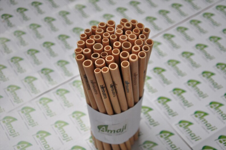May include: A bundle of brown bamboo straws with the text "bambustro" printed on them. The straws are arranged in a circle and are sitting on a white surface with a green and white logo that says "Amail".