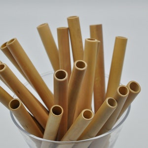May include: A close-up of a glass filled with a bundle of natural brown bamboo drinking straws.