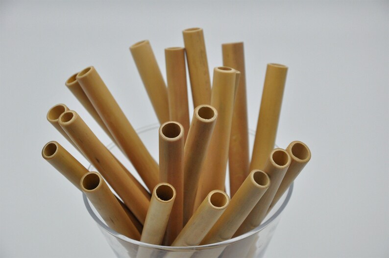 May include: A close-up of a glass filled with a bundle of natural brown bamboo drinking straws.
