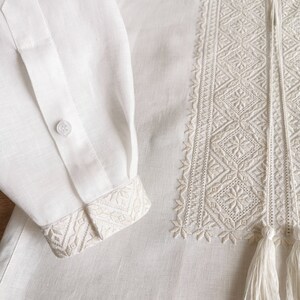 May include: White linen shirt with embroidered detail and a tassel. The embroidery is a geometric pattern in a lighter shade of white.
