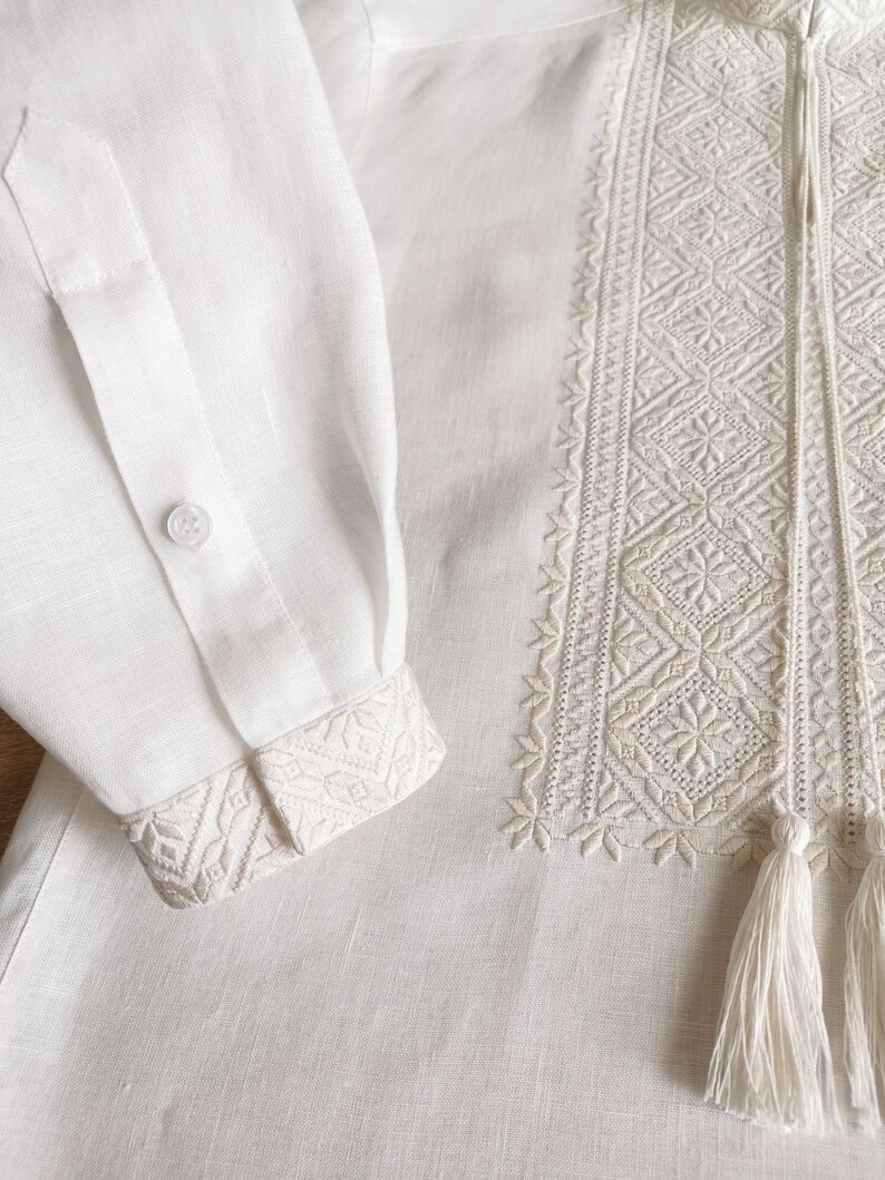May include: White linen shirt with embroidered detail and a tassel. The embroidery is a geometric pattern in a lighter shade of white.