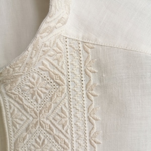 May include: White linen shirt with intricate embroidered details around the collar and neckline.