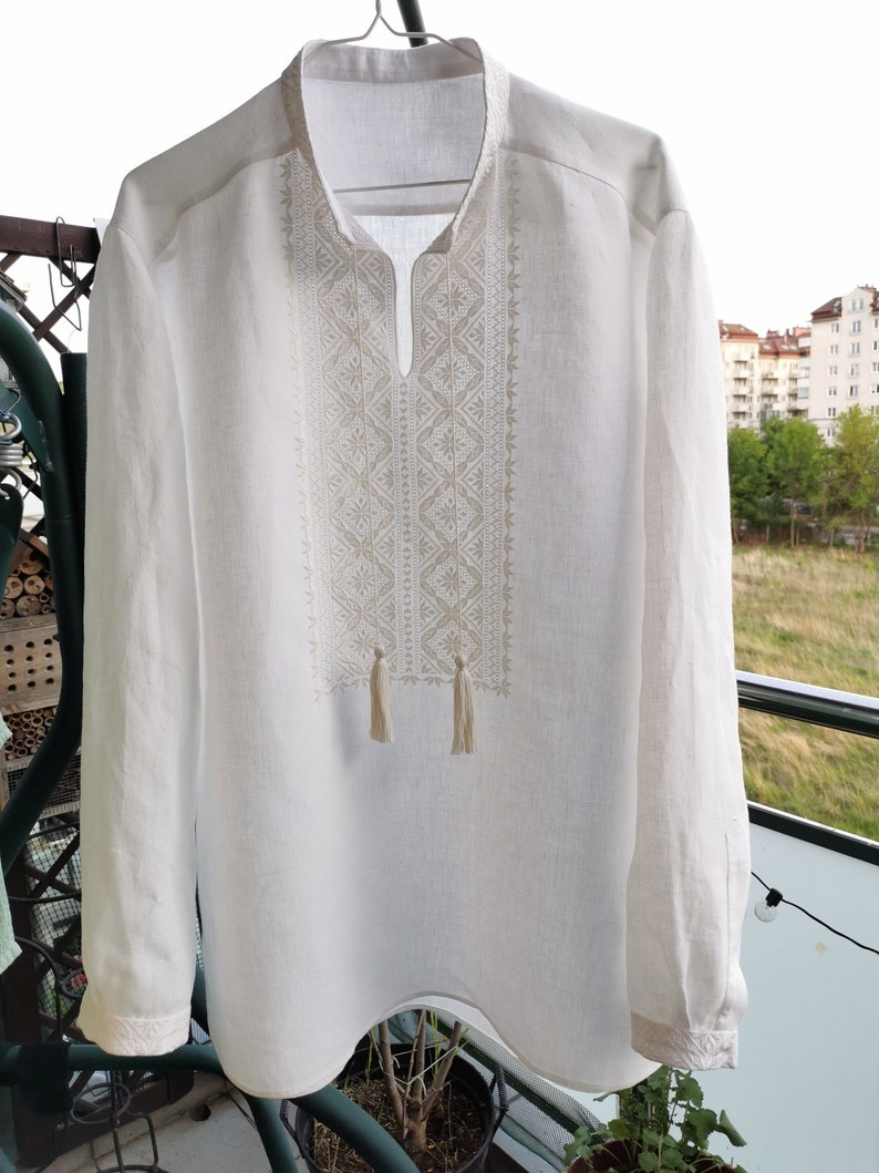 May include: White linen shirt with embroidered geometric pattern and tassels.