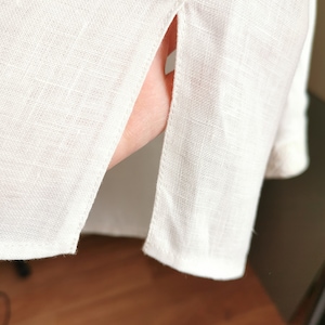 May include: White linen shirt with a side slit detail. The shirt is made of a lightweight fabric and has a relaxed fit.