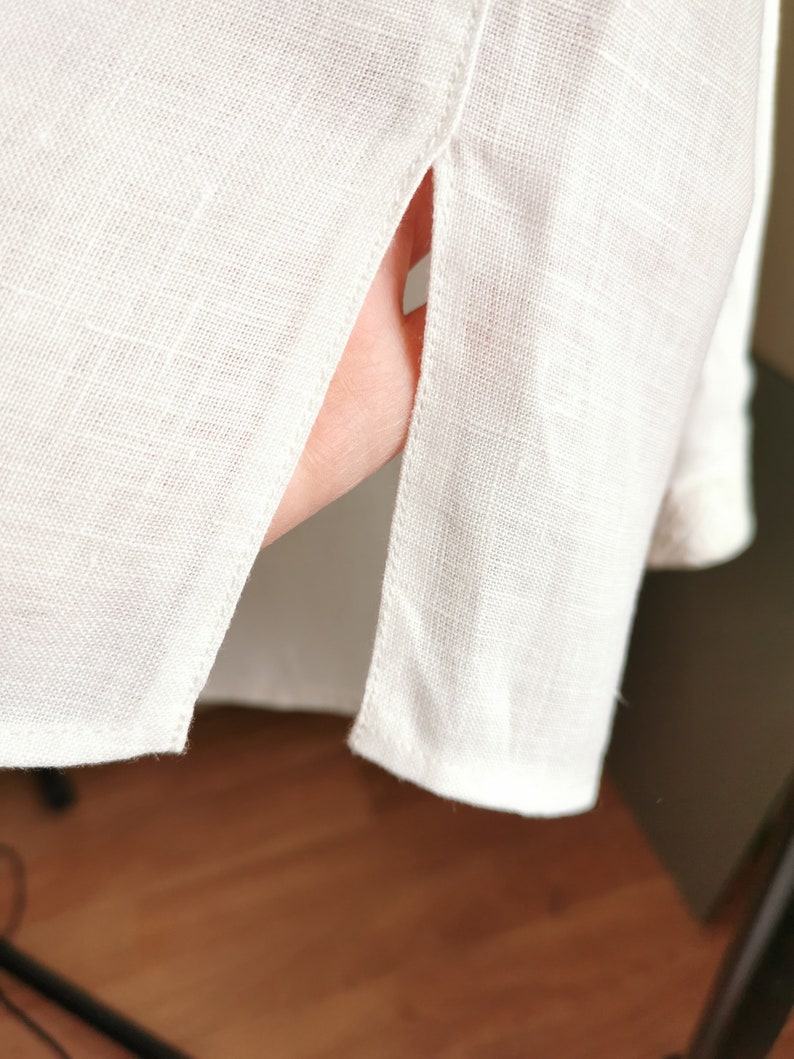May include: White linen shirt with a side slit detail. The shirt is made of a lightweight fabric and has a relaxed fit.